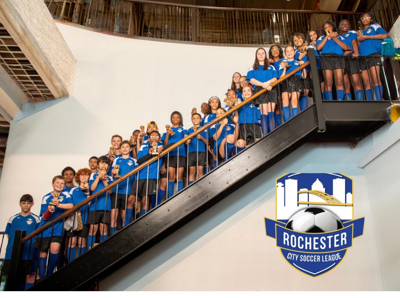 RCSL travel players in blue jerseys with trophies on a staircase